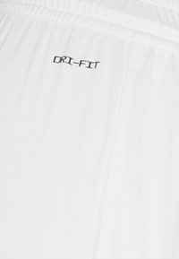 Valkoiset Dri-Fit shortsit, joissa on teksturoitu, hengittävä kangas. Ominaisuuksiin kuuluu joustava vyötärönauha ja pieni brodeerattu "DRI-FIT" -logo mustana.