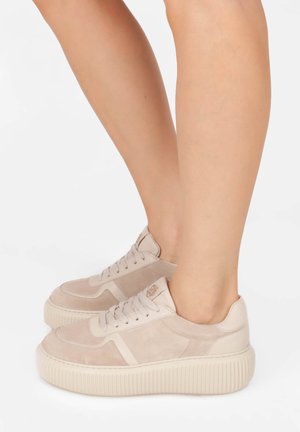 Beige Wildlederschuhe mit einer strukturierten Plattformsohle, runden Schnürsenkeln, gestickten Akzenten und einem Logo-Detail an der Seite.