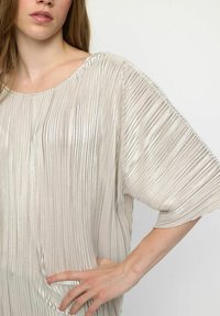 Glanzende, licht zilveren top met geplooide structuur, ruime mouwen en een ronde hals. Het ontwerp heeft een losse pasvorm en zachte draping.