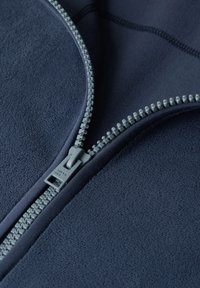 Granatowa polarowa kurtka z szarym zamek błyskawicznym z przodu, z teksturowanym materiałem i przeszytymi panelami wzdłuż kołnierza i zamka.