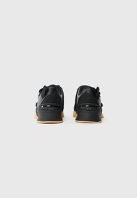 Et par sorte sneakers med gummisåler vist fra bagenden på en ensfarvet hvid baggrund, mærket "L-2" på hæle.