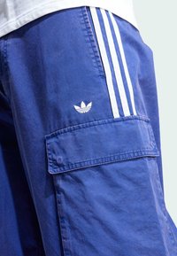 Blå cargo-shorts i texturerat tyg, med vita vertikala ränder och en broderad logotyp på vänstra fickan.