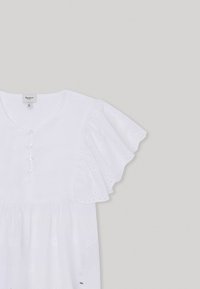 Blusa di cotone bianca con motivi floreali ricamati, maniche corte a volant e cinque bottoni davanti, con vita arricciata.