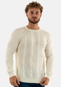 Maglione color crema a maglia intrecciata con scollo a girocollo, dotato di polsini e orlo a coste e un motivo testurizzato su tutta la superficie.