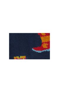 Buntes Strickgewebe mit einem roten Stiefel mit gelben und orangefarbenen Streifen auf dunkelblauem Hintergrund, durchsetzt mit kleinen bunten Blöcken.