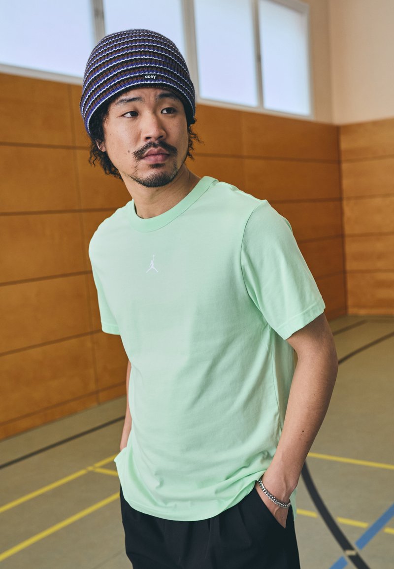Myntegrøn bomulds T-shirt med korte ærmer og rund halsudskæring, prydet med et lille hvidt Jumpman-logo. Sorte løstsiddende bukser og en stribet bærehue.