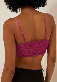 Bralette fucsia corto con texture arricciata, spalline regolabili lucide e schiena elasticizzata, abbinato a pantaloni neri a vita alta.
