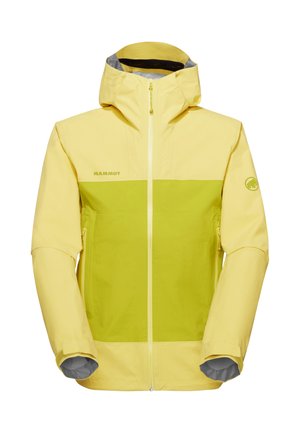 Mann trägt eine gelb-grüne Zip-Up-Jacke mit zwei Fronttaschen, schwarze Hose mit Logo, steht vor einem schlichten grauen Hintergrund.