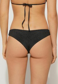 Černé bikini kalhotky s třpytivou texturou, nízkým páskem a detaily na zavazování na bocích, s hladkým povrchem a minimalistickým stylem.