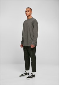 Langärmliges, graues Baumwollhemd mit fransigem Saum, kombiniert mit dunklen, schmal geschnittenen Hosen und schwarzen Vans Sneakers mit weißen Akzenten.