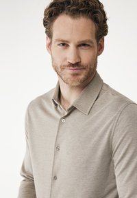 Polo à manches longues de couleur beige, fabriqué dans un tissu doux, avec un col et trois boutons sur le devant. Texture lisse.