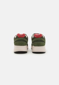 Green suede athletic shoes with a red heel accent, mesh detailing, and a cushioned white midsole; black rubber outsole.
