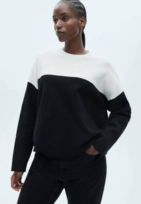 Black and white color-blocked sweater made from knitted fabric. Features a round neckline and long sleeves, with ribbed cuffs and hem.