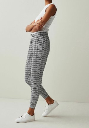 Pantaloni jogger a fantasia bianco e nero con vita regolabile, vestibilità affusolata e tessuto liscio, abbinati a sneaker bianche e un top a canotta bianco aderente.