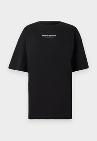 Čierne oversized tričko vyrobené z bavlny, s okrúhlym výstrihom a krátkymi rukávmi, s nápisom "STUDIO EDITION" v bielej farbe.