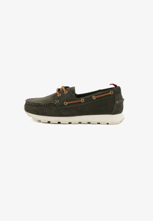 Scarpa da barca in camoscio verde scuro con suola bianca, lacci in pelle marrone infilati attraverso occhielli dorati e linguetta in tessuto rossa sul tallone.