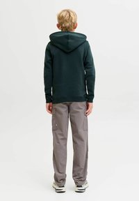 Sudadera con capucha de color verde oscuro con bolsillo tipo canguro y cordón ajustable. Combinada con pantalones cargo de color gris claro que cuentan con bolsillos laterales y detalles cosidos.