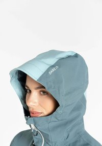 Türkiser Kapuzenjacke mit einem hellblauen Akzent, Reißverschluss und Logodetail. Glatte Textur mit einem strukturierten Design für den Einsatz im Freien.