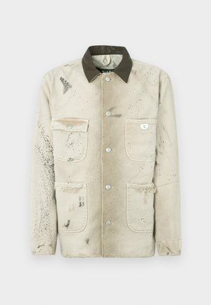Chaqueta de lona beige con un cuello oscuro, cuatro bolsillos, botones plateados y una textura desgastada con detalles de salpicaduras de pintura.