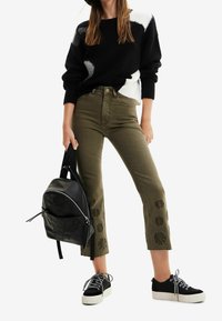 Sweter w czarno-biały wzór, oliwkowozielone krótkie dżinsy z kwiatową haftem, czarny sk�órzany plecak oraz czarne trampki z białymi podeszwami.