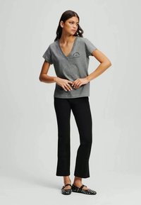 Γκρι βαμβακερό μπλουζάκι με V λαιμόκοψη και κοντά μανίκια, που διαθέτει εκτύπωση κειμένου. Φορεμένο με μαύρα φαρδιά παντελόνια και μαύρα φλατ παπούτσια με τρουκς.