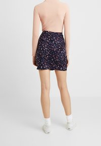 Kvinna som står vänd bort, iklädd en rosa ribbad långärmad topp, marinblå blommig minikjol, vita strumpor och vita sneakers.