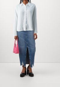 Camicia azzurro chiaro a maniche lunghe, gonna di jeans con spacchi frontali, scarpe con tacco nere e una piccola borsa rosa. Tessuto morbido e dettagli con orlo sfilacciato.