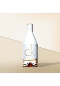 Hvit glassflaske med en avsmalnet form, gulldetaljer og preget "ck"-logo. Klar bunn viser en brun væske inni.