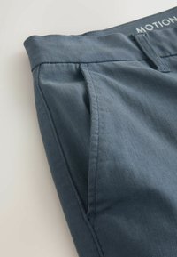 Kék nadrág texturált anyagból, lapos elejű, oldalzsebekkel, és "MOTION" feliratú derékpánttal. Tiszta varrási részletek.