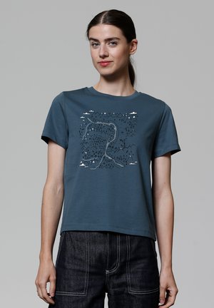 T-shirt à manches courtes, couleur teal, avec un imprimé graphique de montagnes, de nuages et d'une rivière sinueuse, fabriqué en coton avec une texture douce.