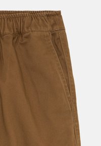 Pantaloni di cotone marroni con cintura elastica, tasche laterali e una superficie liscia. Il tessuto presenta un sottile motivo a trama diagonale.