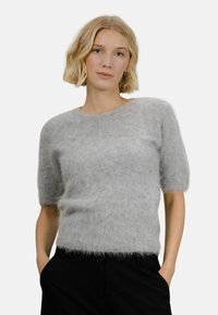Lysegrå kortermet genser laget av luftig, mykt materiale med rund hals og avslappet passform. Brukt sammen med mørke bukser.