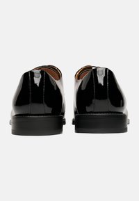 Schwarze Lacklederschuhe mit glatter Oberfläche, runder Zehenform und minimaler Naht. Dicke schwarze Sohlen mit polierter Optik.