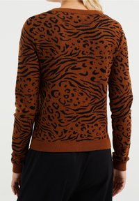 Brun tröja med svart tigerrand och leopardfläckar. Har en rund halsringning och ribbade muddar och nederkant. Mjuk stickad textur.