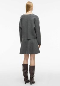 Šedý svetr ze směsi vlny s kleslými rameny spárovaný s rozšířenou sukní, doplněný hnědými koženými kozačkami po kolena.