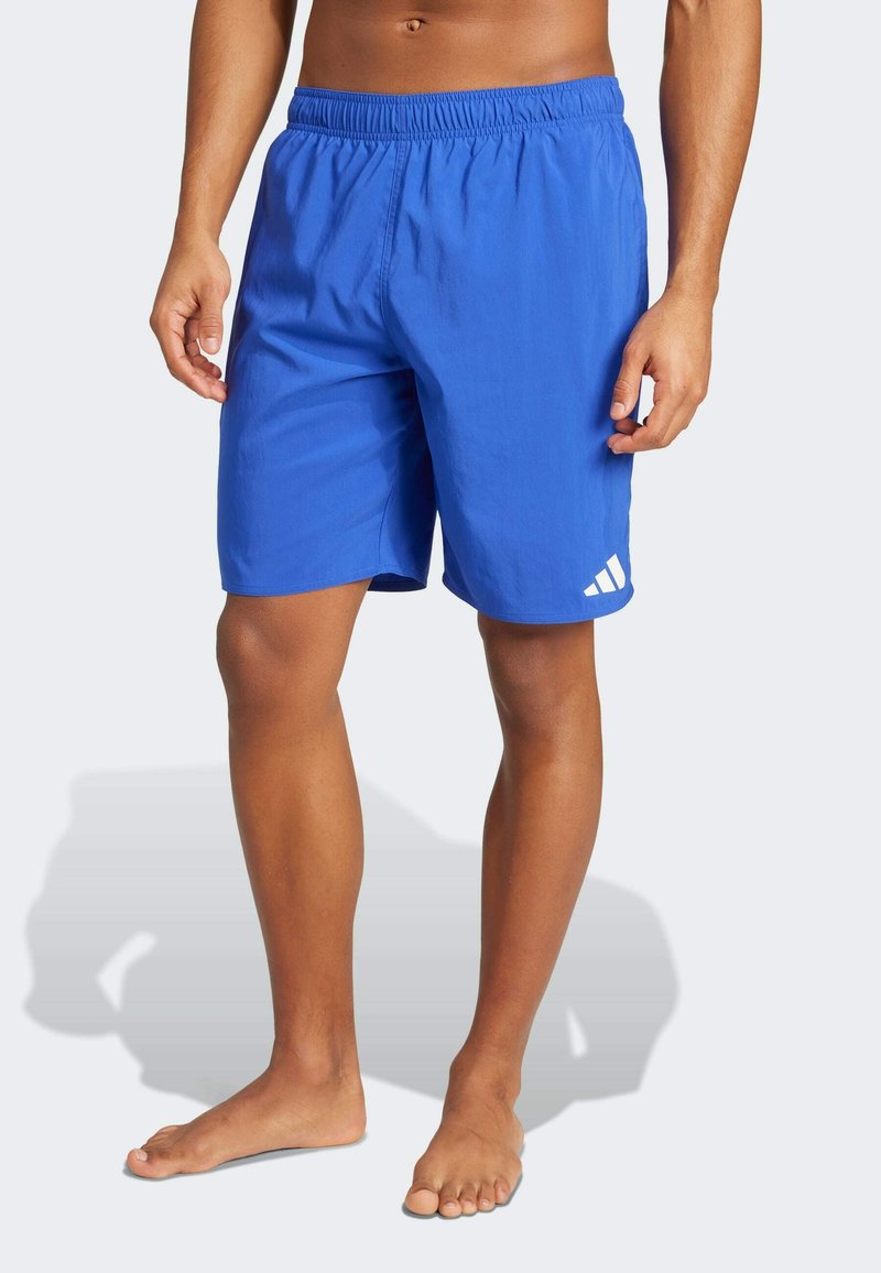 Bañador deportivo azul con cintura elástica, textura suave y un acento de logo blanco en la parte inferior de la pierna izquierda.