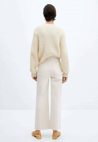 Suéter de punto beige claro con un ajuste holgado, combinado con pantalones de pierna ancha en color blanco roto. La textura es suave; ambas prendas tienen un diseño minimalista.