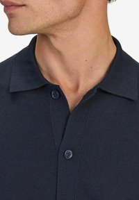 Mörkblå stickad polo med krage och två framknappar, med en slät textur och subtilt vävt mönster.