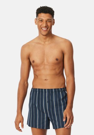 Herren-Badeshorts in Marineblau mit vertikalen Streifen. Elastischer Taillenbund mit Kordelzug. Leichter Stoff mit glatter Textur.