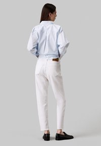 Camicia a righe blu chiaro con una vestibilità comoda e spalle scese, abbinata a pantaloni bianchi a gamba dritta e scarpe nere slip-on.