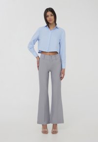 Camicia corta azzurra con bottoni e maniche lunghe abbinata a pantaloni grigi chiari a sbuffo, attillati, con dettagli a doppio bottone e tessuto testurizzato.