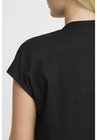 Top nero a maniche corte con vestibilità rilassata, caratterizzato da un semplice scollo rotondo e tessuto testurizzato. Il retro è semplice e privo di decorazioni.