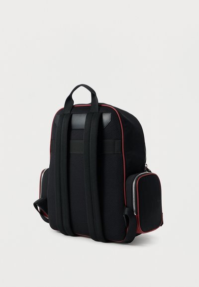 Μαύρο σακίδιο με επενδεδυμένους ιμάντες ώμου, πλέγμα στην πλάτη, πλαϊνές τσέπες με φερμουάρ και κόκκινη διακόσμηση σε απλό ανοιχτό φόντο.