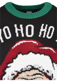 Pull en maille noire avec col vert, arborant le texte blanc "HO HO HO" et une illustration partielle du Père Noël en rouge et blanc.