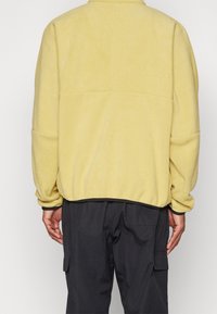 Gul fleecejacka med avslappnad passform, med hög krage och elastiska muddars, i kombination med mörka cargobyxor.