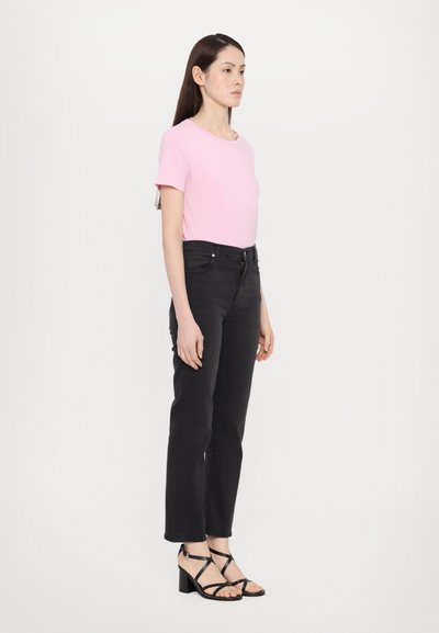 T-shirt rosa chiaro a maniche corte, jeans in denim neri e sandali con tacco strappy neri. L'outfit presenta un design semplice e aderente.