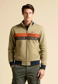 Giacca khaki con zip, caratterizzata da strisce blu e arancioni, con toppe di testo, polsini a coste e colletto rotondo. Tessuto morbido.
