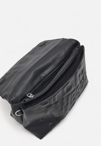 Sac bandoulière en cuir noir avec lettres embossées, rabat ouvert et poche zippée visible à l’intérieur sur fond blanc.
