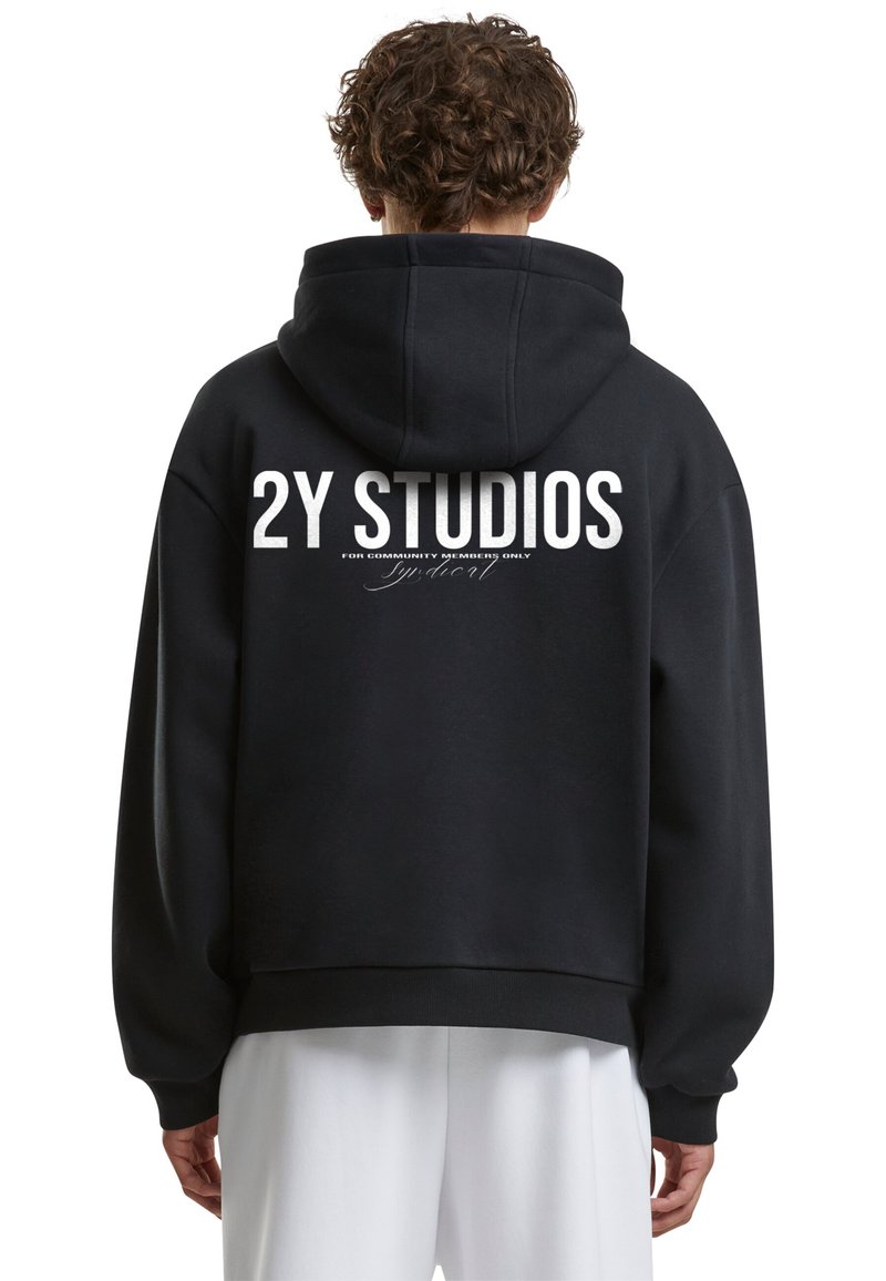 Juoda su kapuce megztinis, kuriame nugaros pusėje yra didelis baltas grafiškas tekstas "2Y STUDIOS", su laisvu kirpimu ir plačiomis rankovėmis.