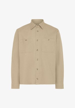 Chemise beige à manches longues avec col pointu et deux poches poitrine, toutes deux fermées par des boutons.